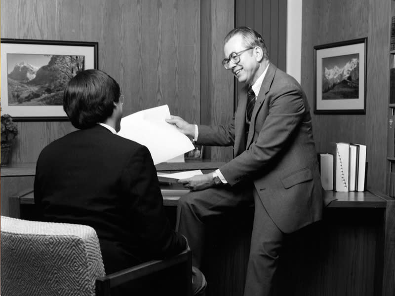 Dr. Zuck seated on a desk talking with a man